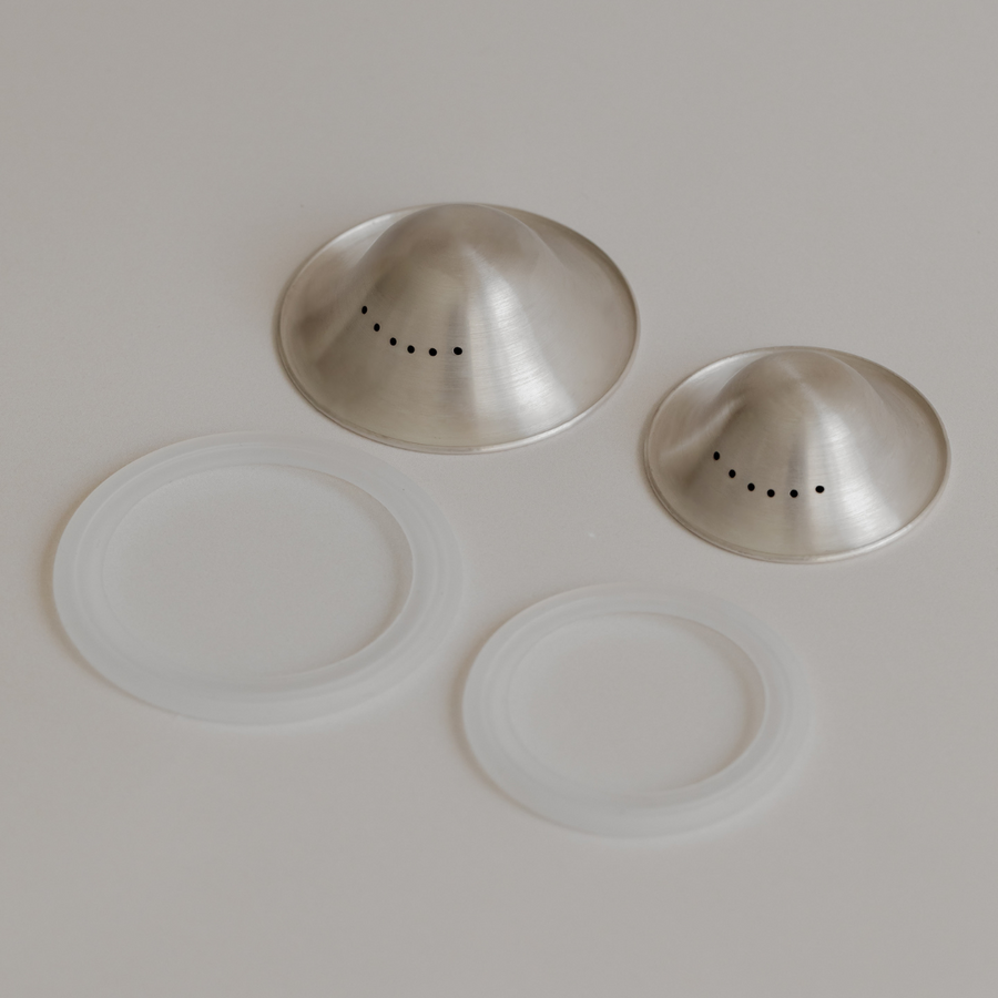 Stainless steel Bosom Ritual™ Objects salt and pepper shakers with their silver plastic lids displayed on a neutral surface by Mammae The Embodied Mother.