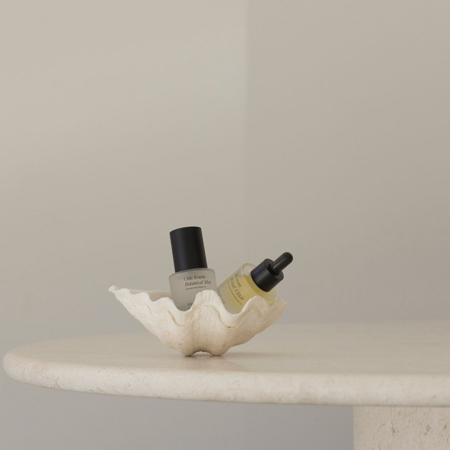A table adorned with a shell and a Mini Ode Form™ Botanical Mist by Mammae The Embodied Mother sitting on top, creating a serene atmosphere for an aromatherapy ritual.