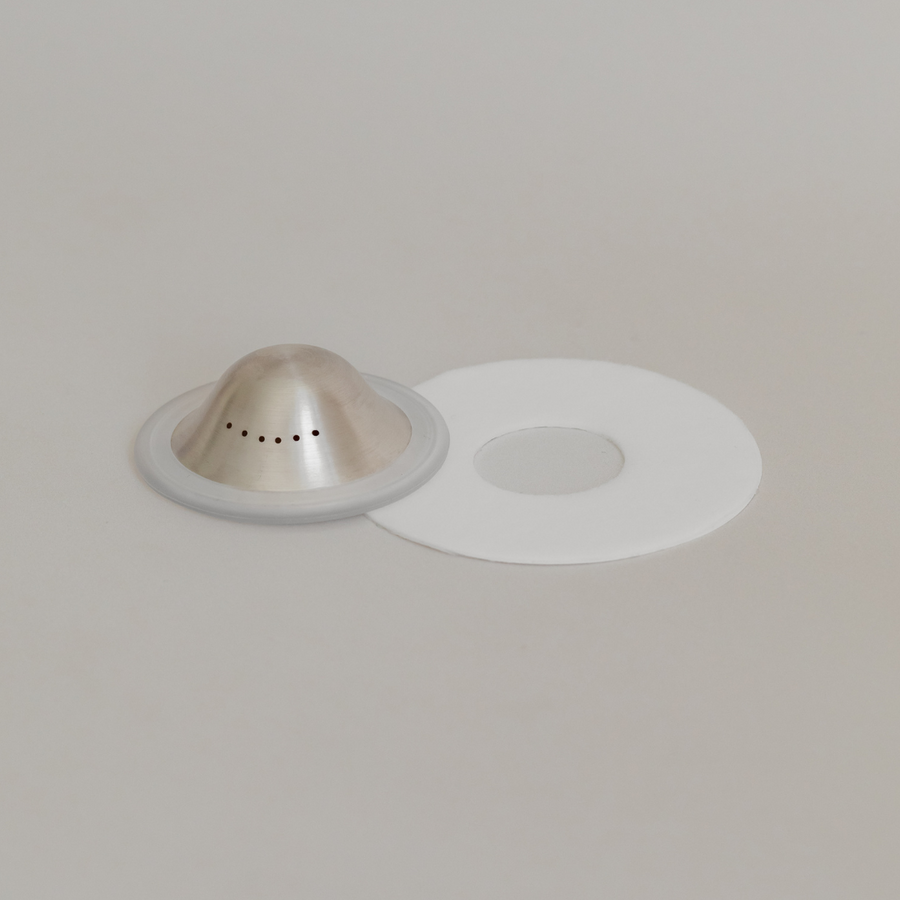 Bosom Ritual™ Discs next to their white rubber gasket with aloe-infused hydrogel adhesives on a neutral background by Mammae The Embodied Mother.