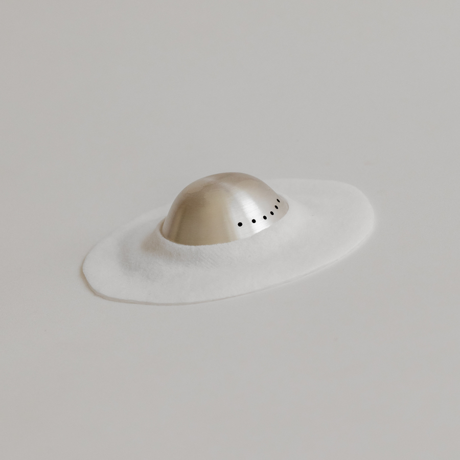 Minimalist representation of a hat using a flat white surface and a three-dimensional semi-spherical object with Mammae The Embodied Mother Bosom Ritual™ Discs details.