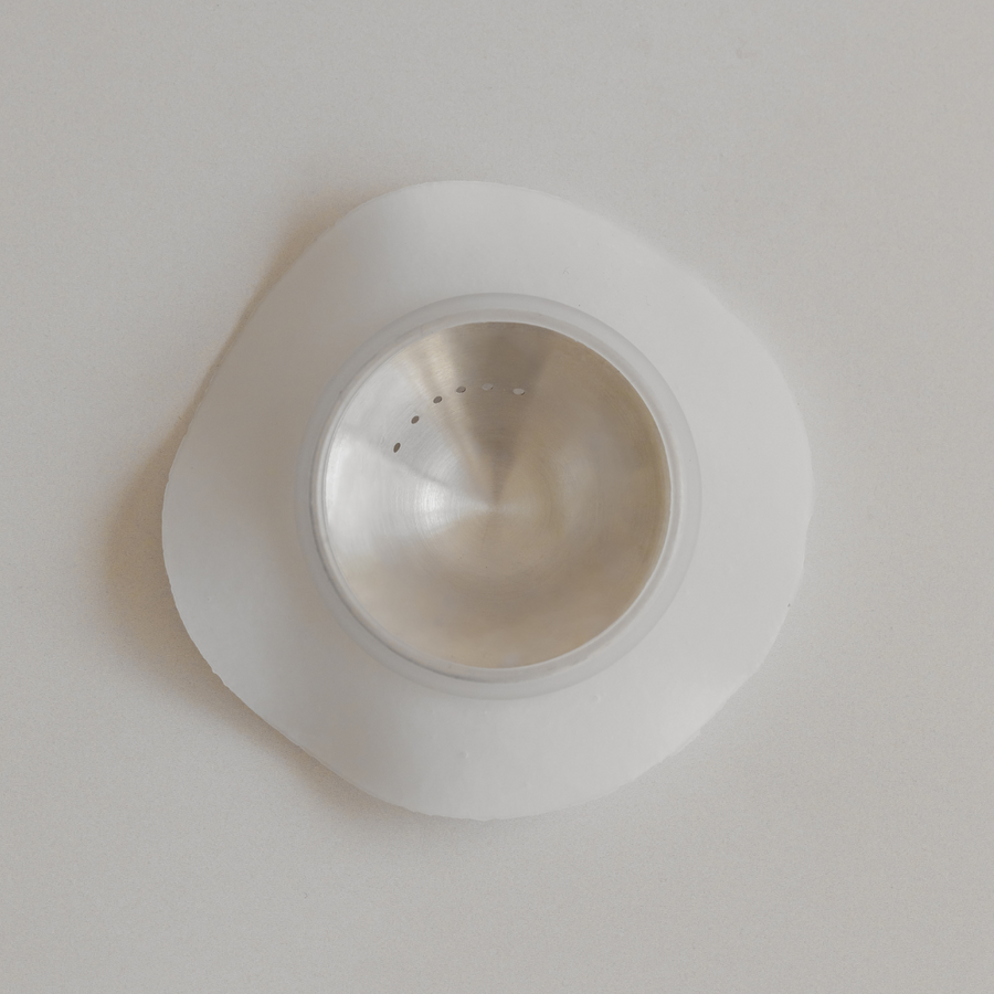 Stainless steel sink strainer on a white surface with Bosom Ritual™ Discs by Mammae The Embodied Mother adhesives.