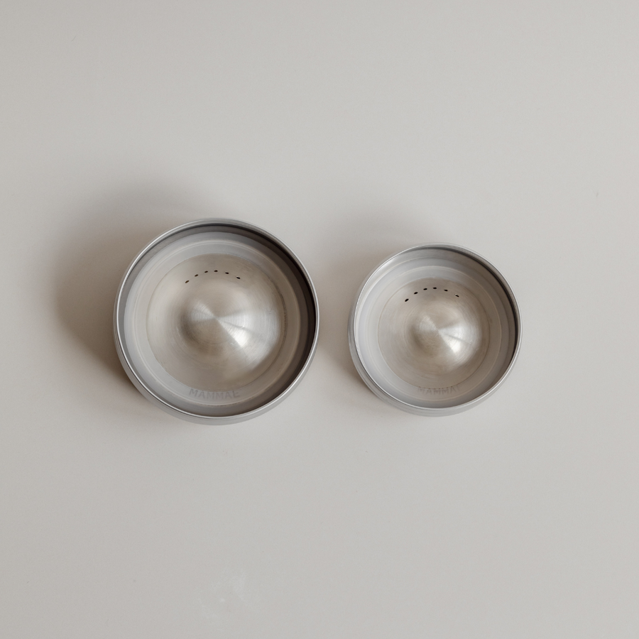 Two empty silver stainless steel Bosom Ritual™ Objects pet bowls on a light surface. (Brand: Mammae The Embodied Mother)
