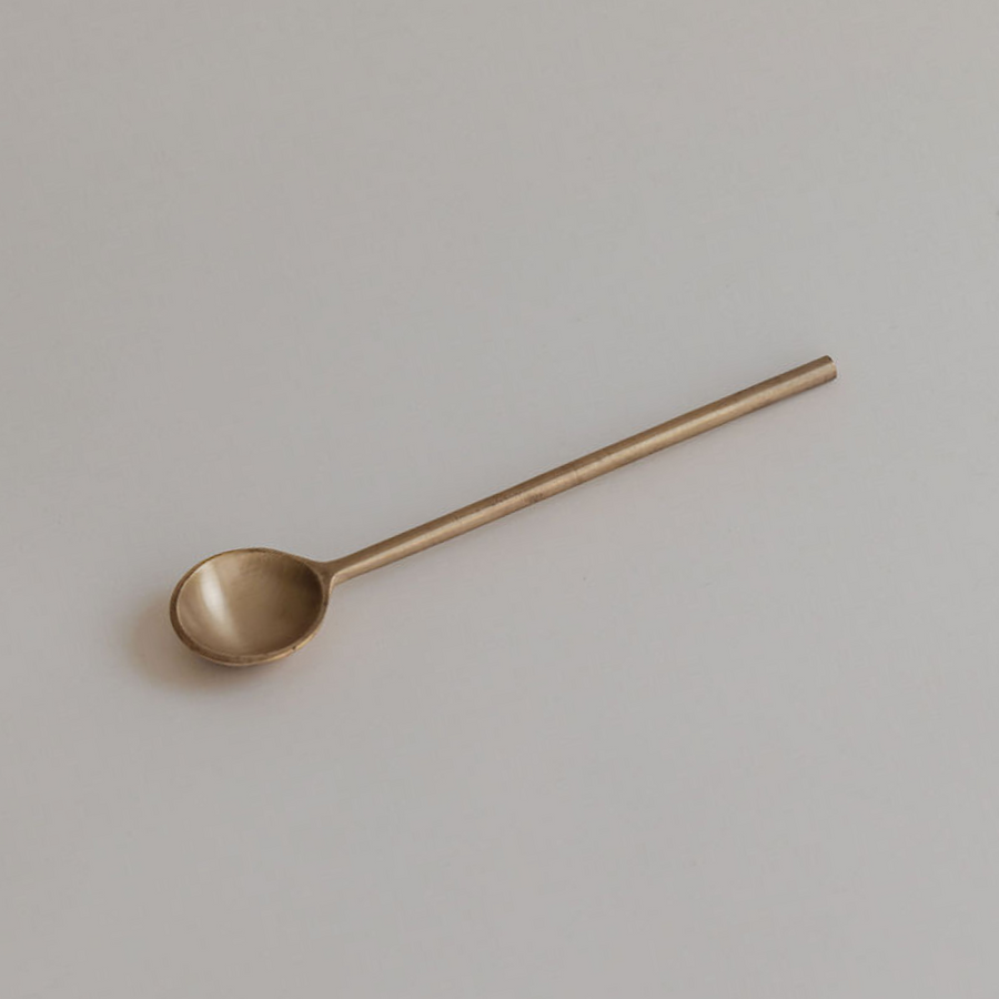 Mammae Ritualware Brass Teaspoon laying flat on a neutral paper backdrop ready to be served with loose leaf organic nursing tea. 