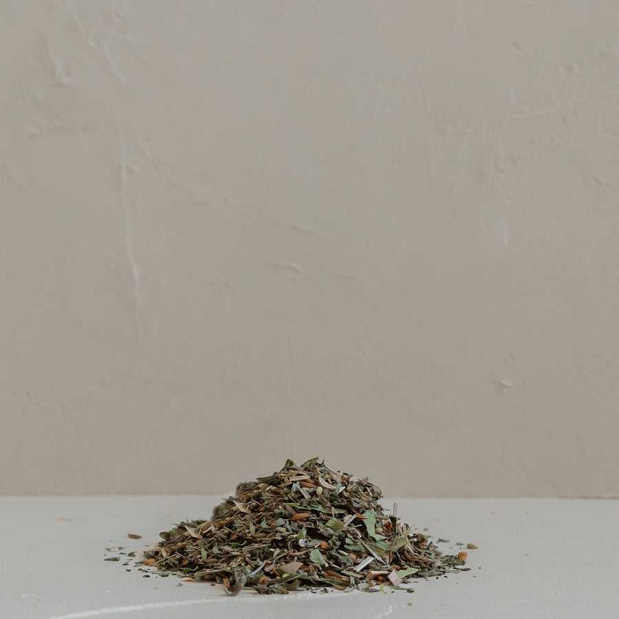 A pile of Mammae The Embodied Mother's Bosom Ritual™ Infusion organic dried herbs on a white table.