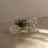 Mammae breastfeeding pyramid tea bag sitting in a vintage glass tea cup and saucer steeping in hot boiling water on a neutral background. 