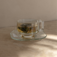 Mammae breastfeeding pyramid tea bag sitting in a vintage glass tea cup and saucer steeping in hot boiling water on a neutral background. 