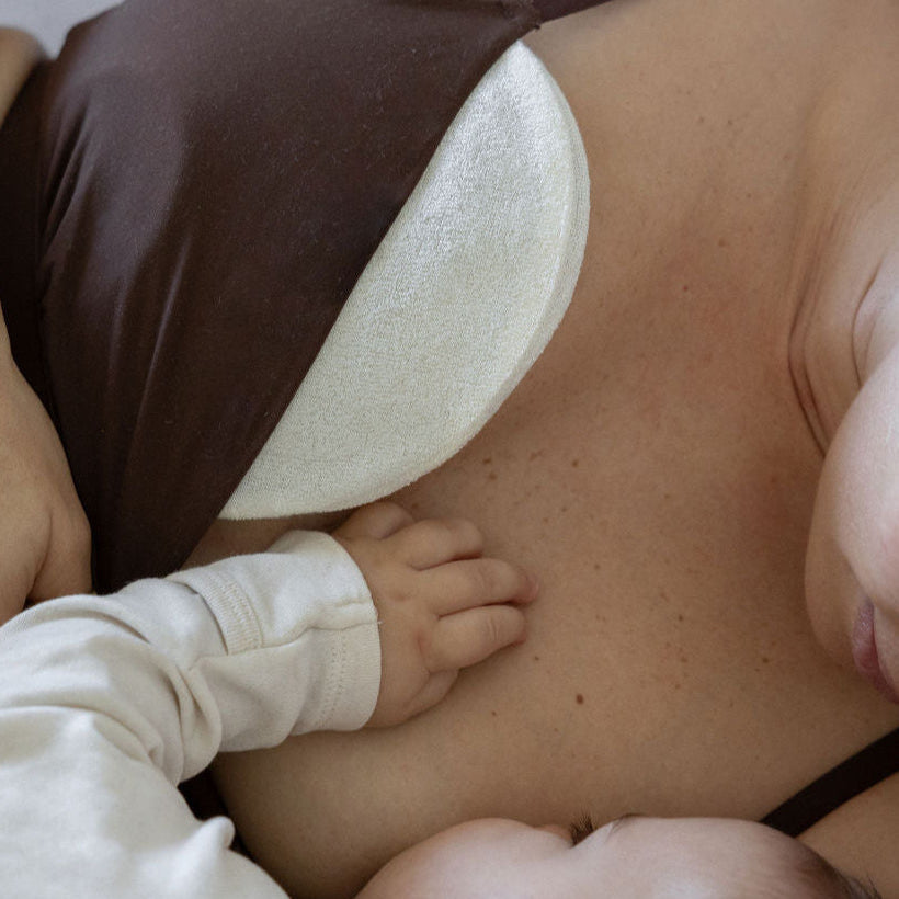 mother breastfeeding a baby using a nursing pillow and hot and cold breast pack by Mammae with organic reusable bamboo cover layered on the skin. 