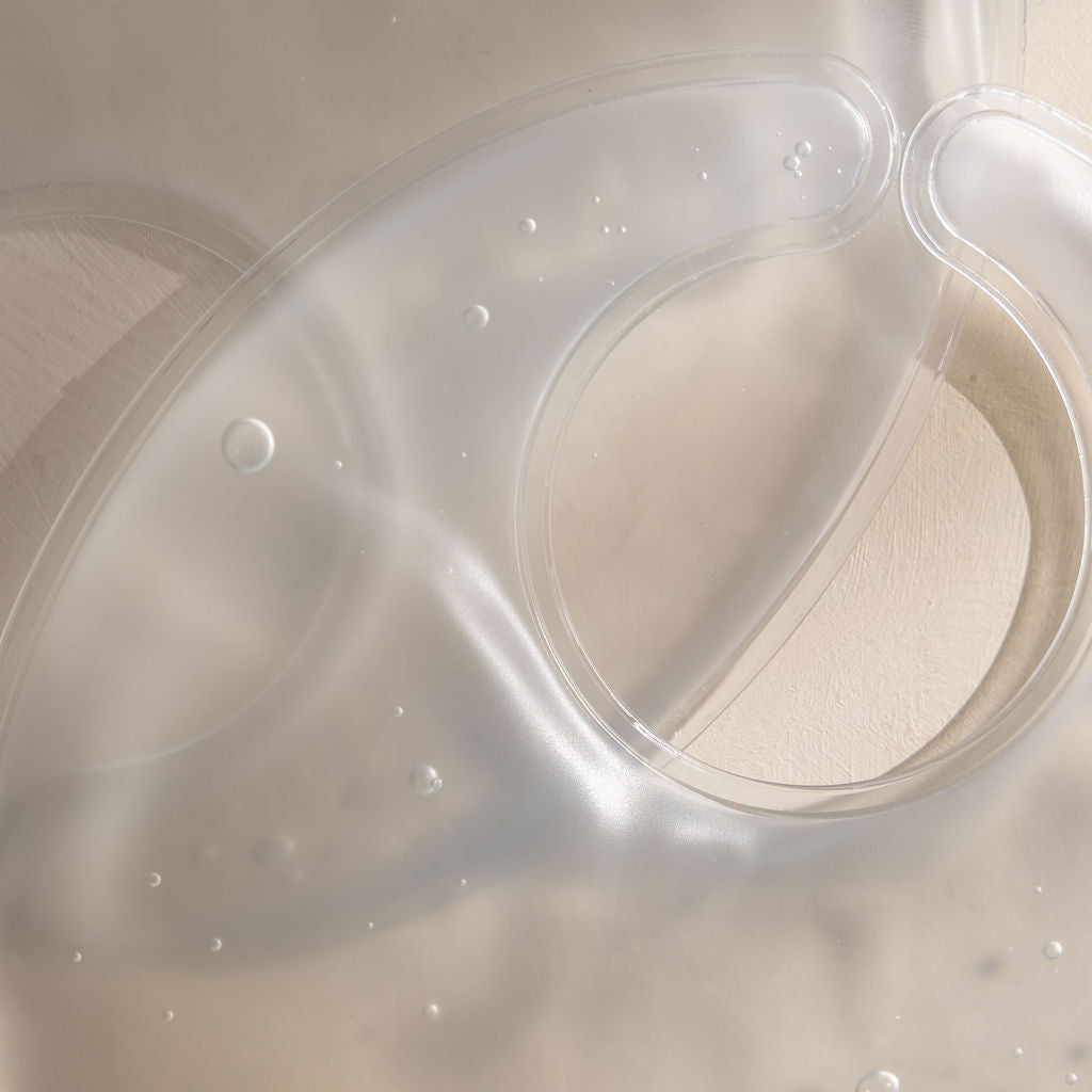 Clear hot and cold breast compress by Mammae with a circular nipple opening on a beige background and glear non-toxic gel. 
