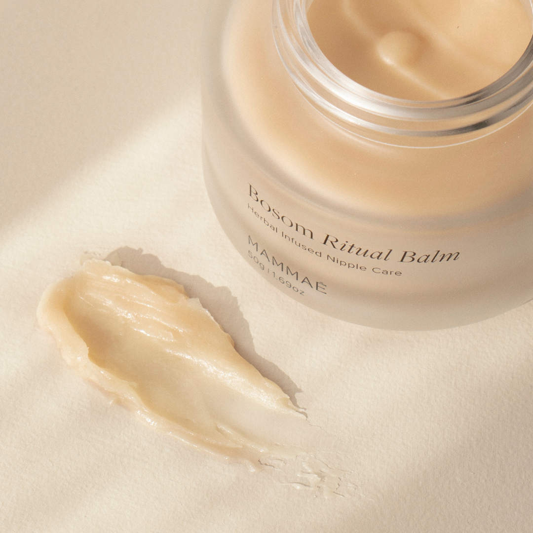A jar of Mammae The Embodied Mother Vegan Bosom Ritual™ Balm, designed for nursing and pregnancy, sitting on a white surface. Vegan nipple balm swatch on neutral surface. Best Nipple Balm Award Winner. 