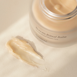 A jar of Mammae The Embodied Mother Vegan Bosom Ritual™ Balm, designed for nursing and pregnancy, sitting on a white surface. Vegan nipple balm swatch on neutral surface. Best Nipple Balm Award Winner. 