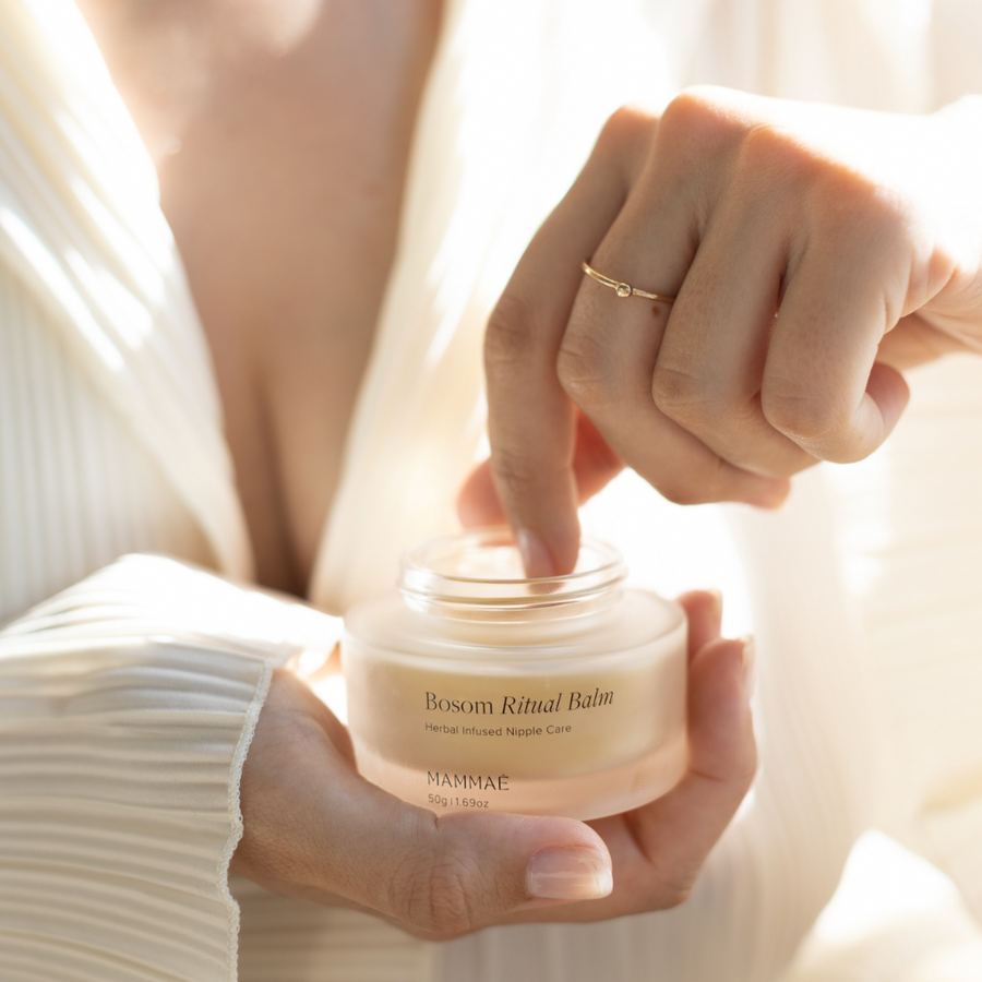 A postpartum mother is holding a glass jar of the Mammae Bosom Ritual™ Balm to apply on her sore, cracked and bleeding nipples that have been damaged from breastfeeding and pumping. Vegan and 100% natural nipple cream made in Australia. 