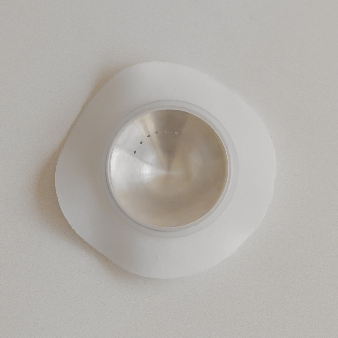 Stainless steel sink strainer on a white surface with Bosom Ritual™ Discs by Mammae The Embodied Mother adhesives.