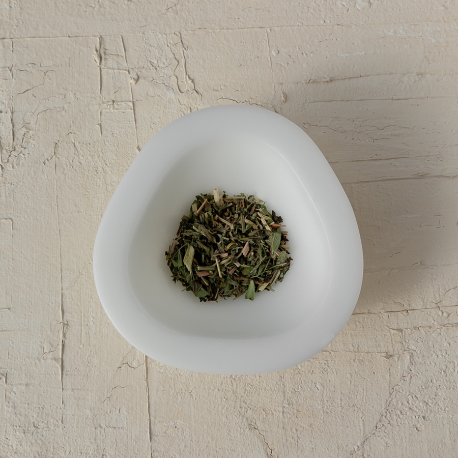 A white bowl filled with Mammae The Embodied Mother's Bosom Ritual™ Infusion, designed for nursing and breast care, on a table.