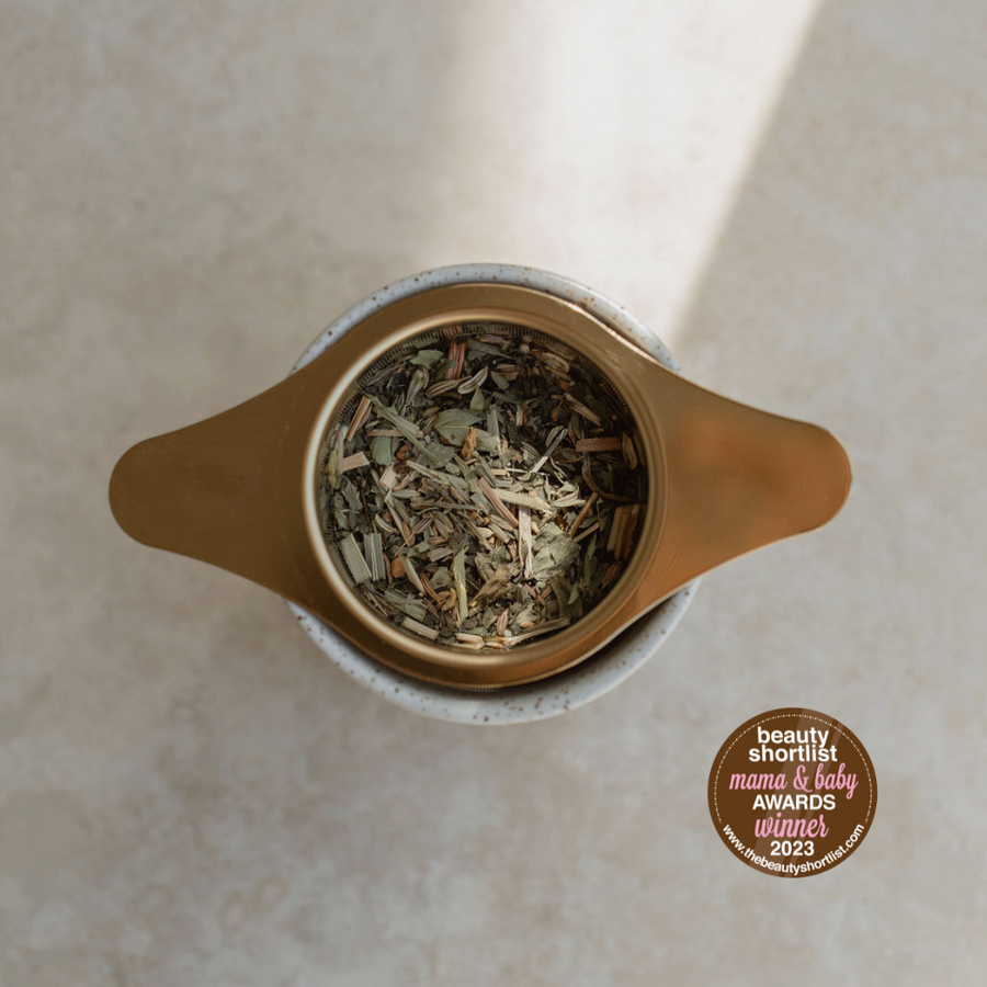 A cup of Bosom Ritual™ Infusion green tea, designed for lactation support during pregnancy and to prevent mastitis, on a table with a lid, by Mammae The Embodied Mother