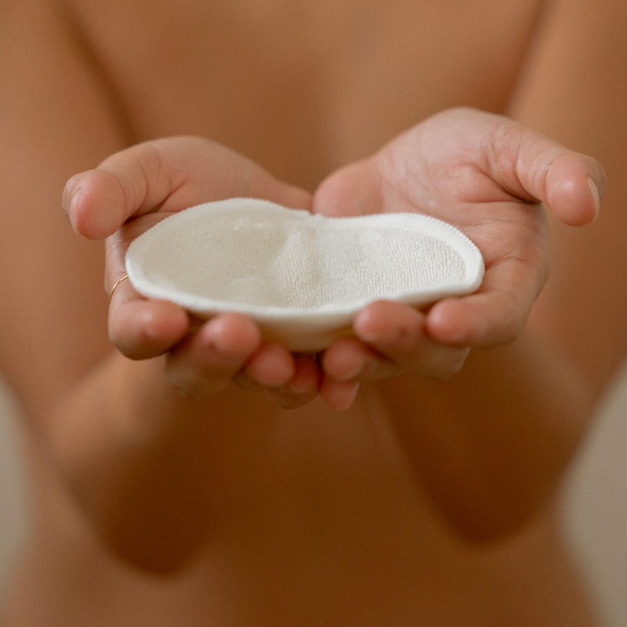 A postpartum mothers hands holding a white Bosom Wearables contoured nursing pad from the brand Mammae for Breastfeeding.