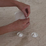 A new mother peeling back the Mammae aloe-infused hydrogel adhesives and sticking them down onto the surface of the breathable silver nipple cups on a travertine kitchen bench top. 