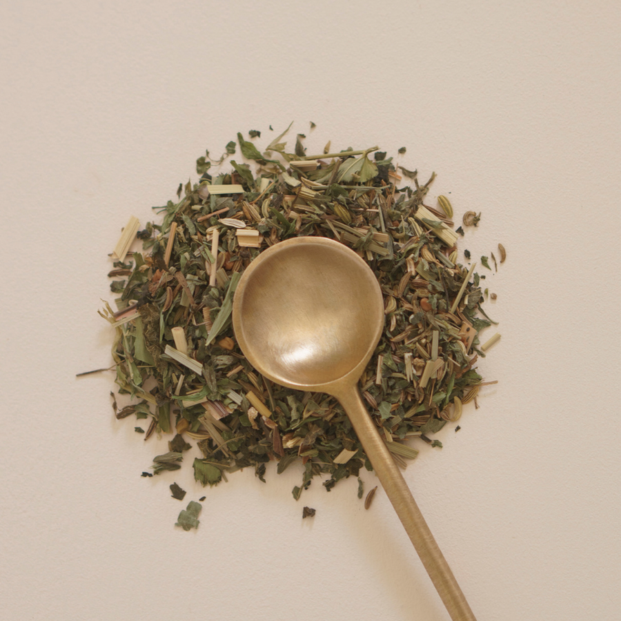 A brass teaspoon from Mammae The Embodied Mother's Ritualware rests on a white surface, symbolizing breast care during pregnancy.