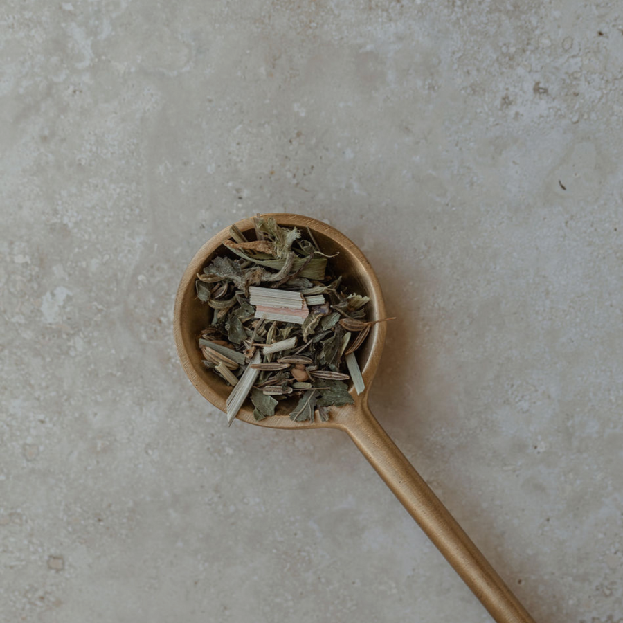 A Ritualware Brass Teaspoon filled with herbs on a stone surface, crafted by Mammae The Embodied Mother for breastfeeding support.