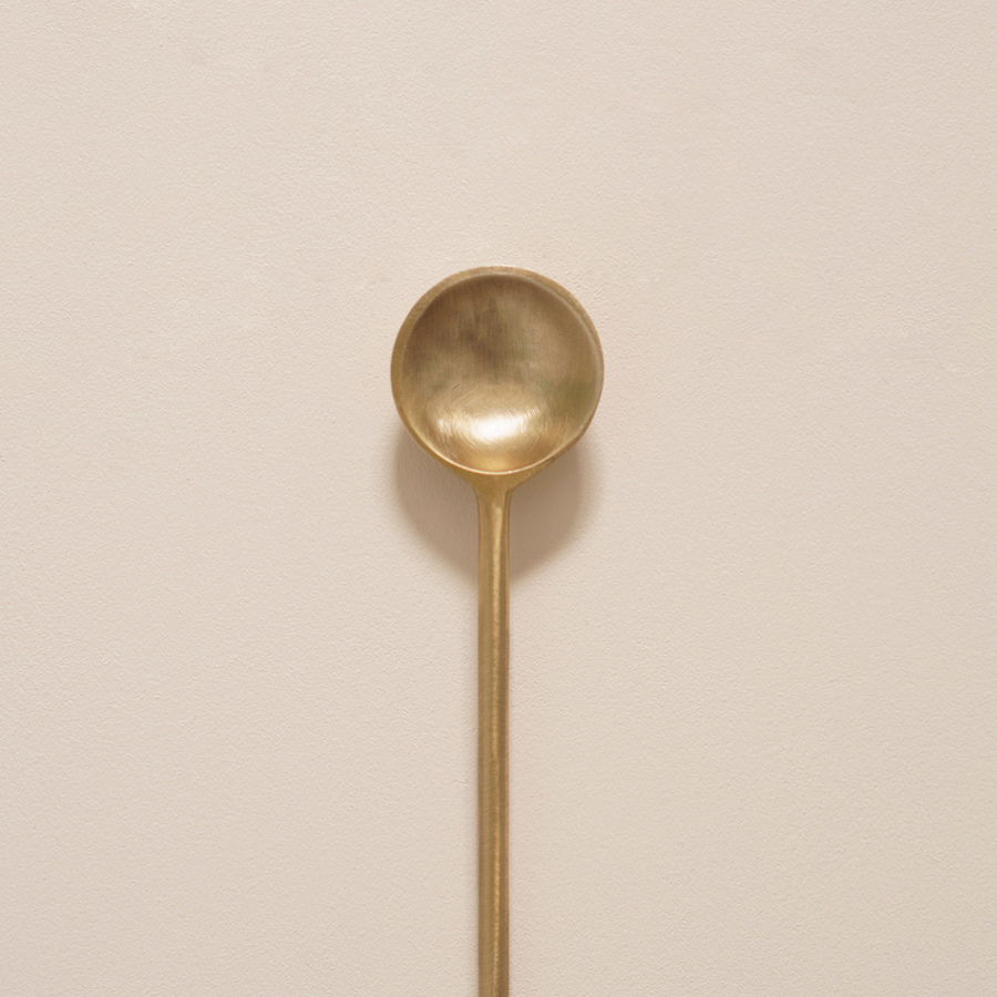 A Brass Teaspoon designed for breastfeeding and nursing, showcased on a beige wall from Mammae The Embodied Mother.