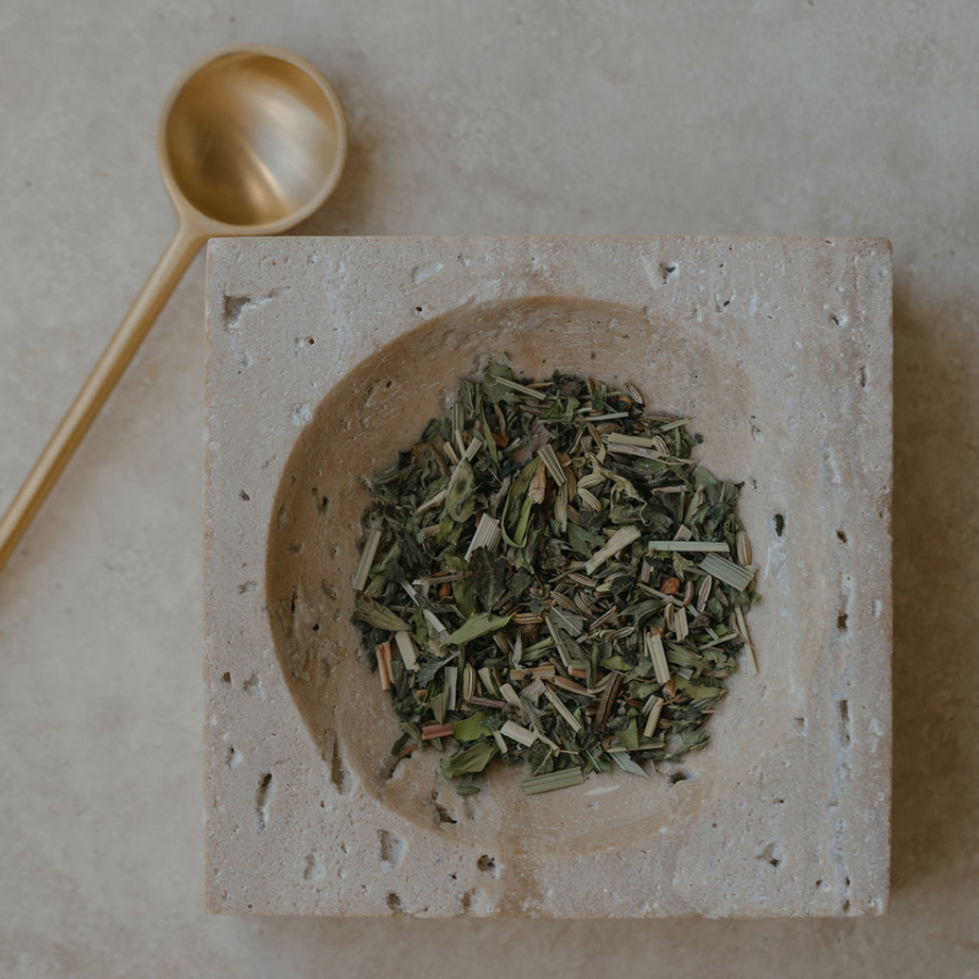 A bowl of Mammae The Embodied Mother green tea for postpartum healing with a Ritualware Brass Teaspoon on top.