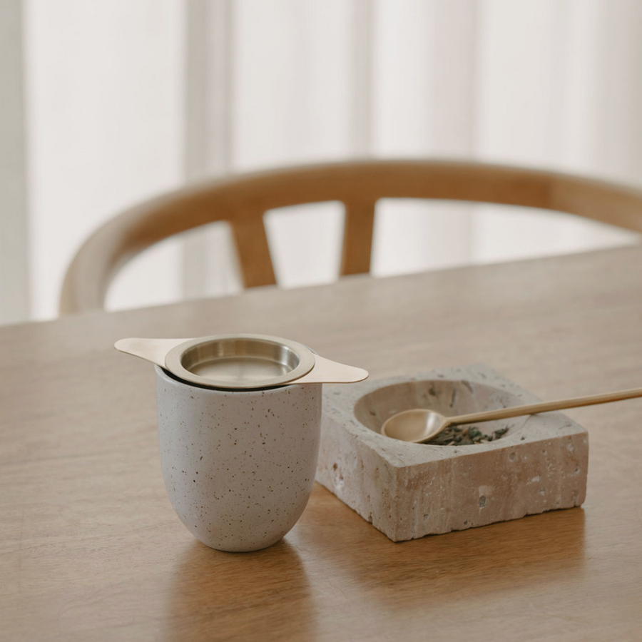 A Ritualware Tea Infuser and a spoon on a wooden table, perfect for postpartum relaxation.