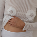Mammae mother wearing a white long sleeve sheer top. Hydrogel adhesives are stuck to blouse to represent size 
